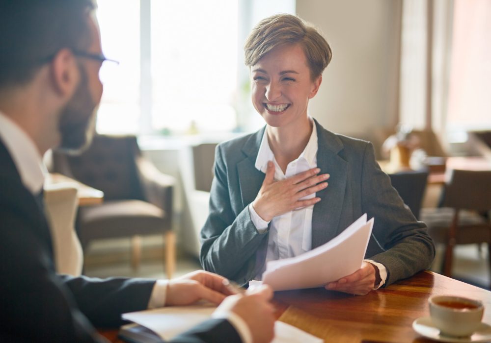 Laughing businesswoman with papers talking to her colleague during meeting in cafe